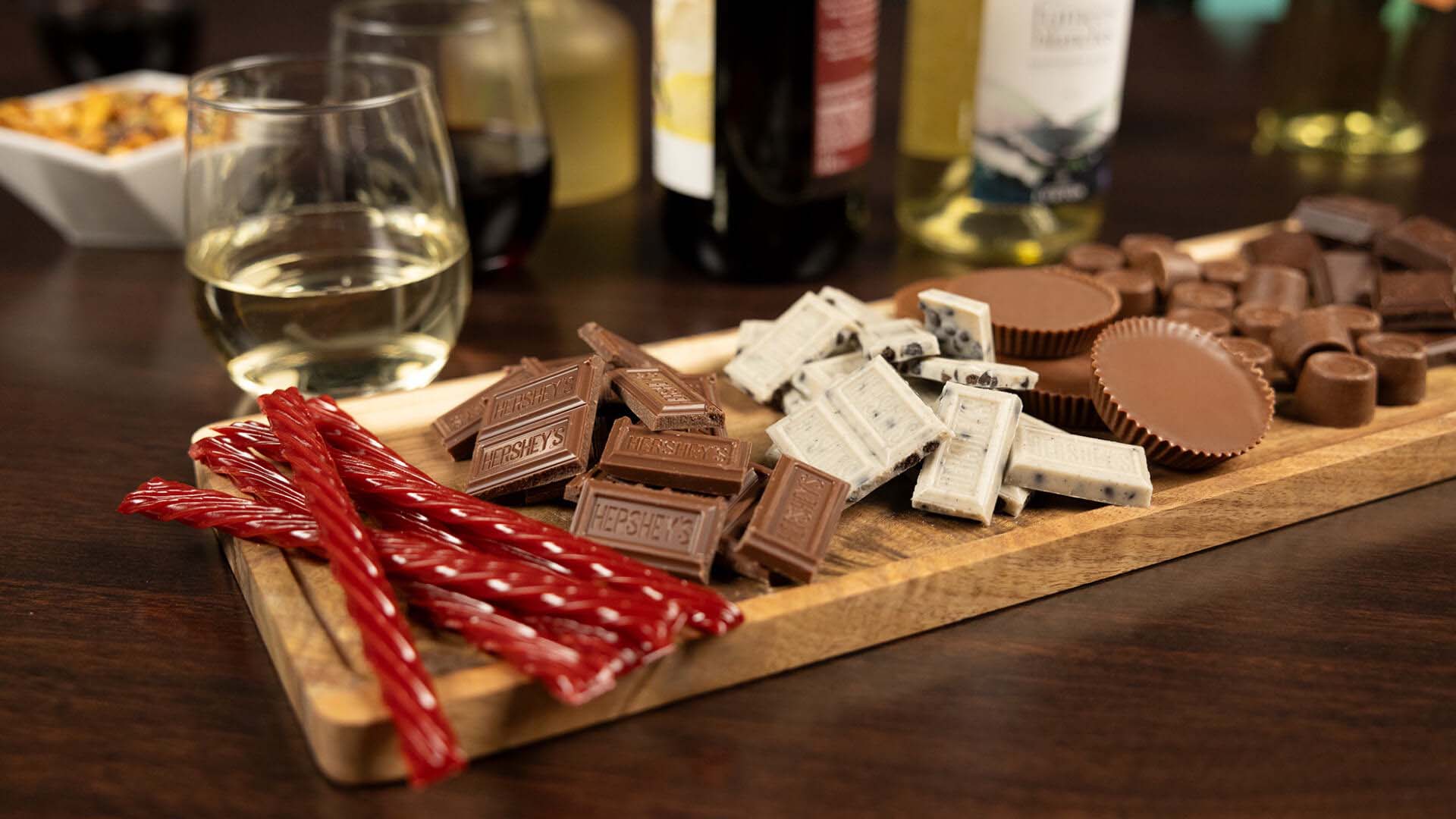 board topped with an assortment of unwrapped hersheys candies beside glasses of wine