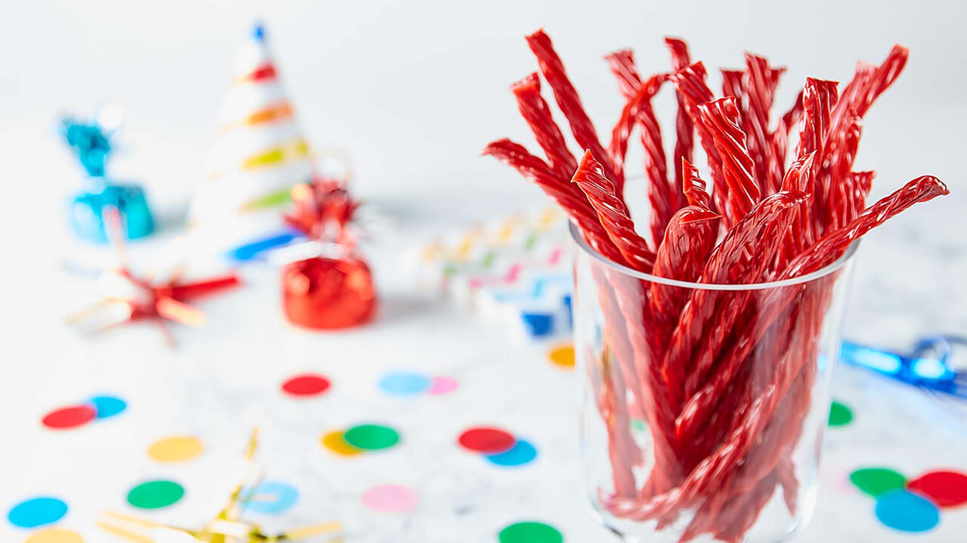 twizzlers strawberry twists inside glass cup surrounded by party decorations