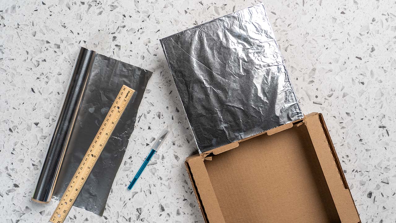 attaching aluminum foil to the lid of the cardboard box