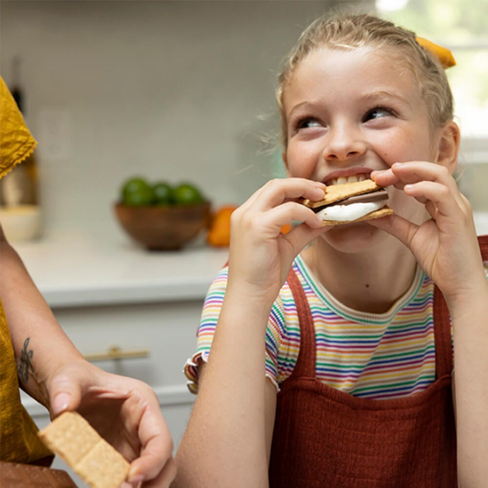 girl enjoying a smore in the kitchen with her parent