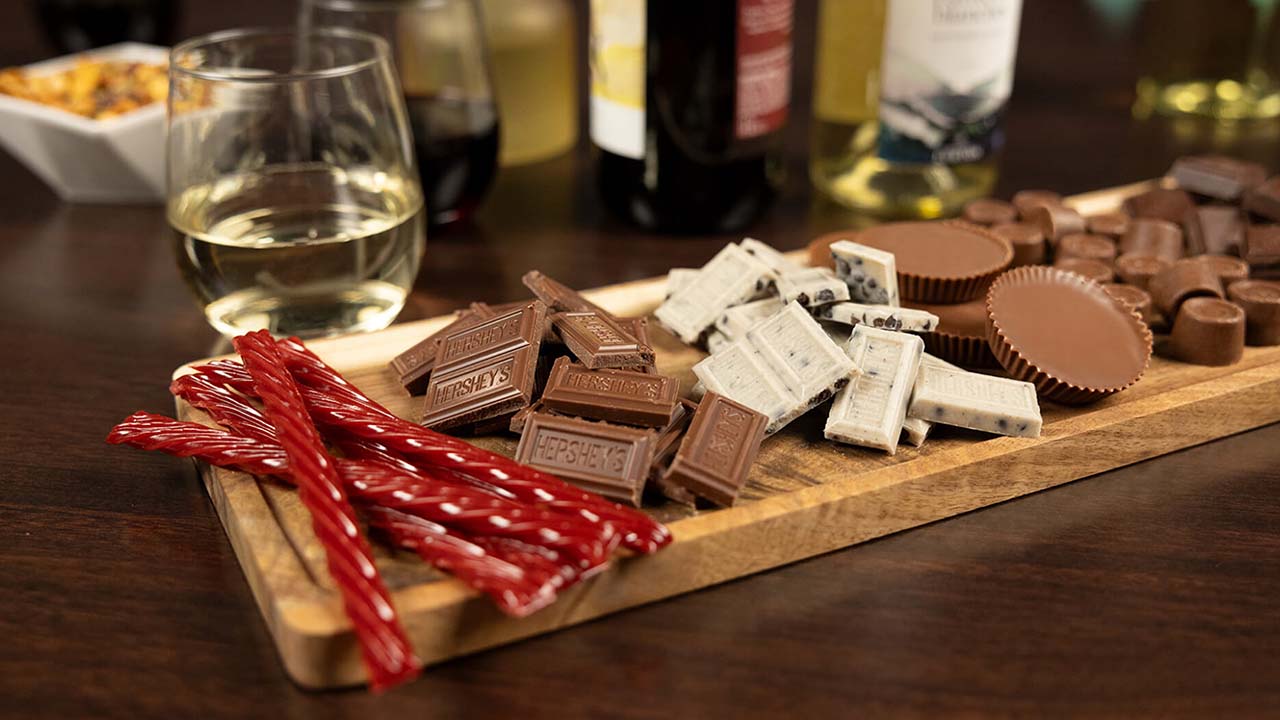 board topped with an assortment of unwrapped hersheys candies beside glasses of wine