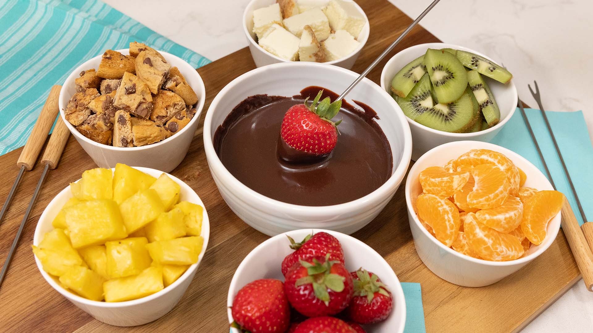 bowls of fresh fruit and cookie and cheesecake bites to dip into chocolate fondue