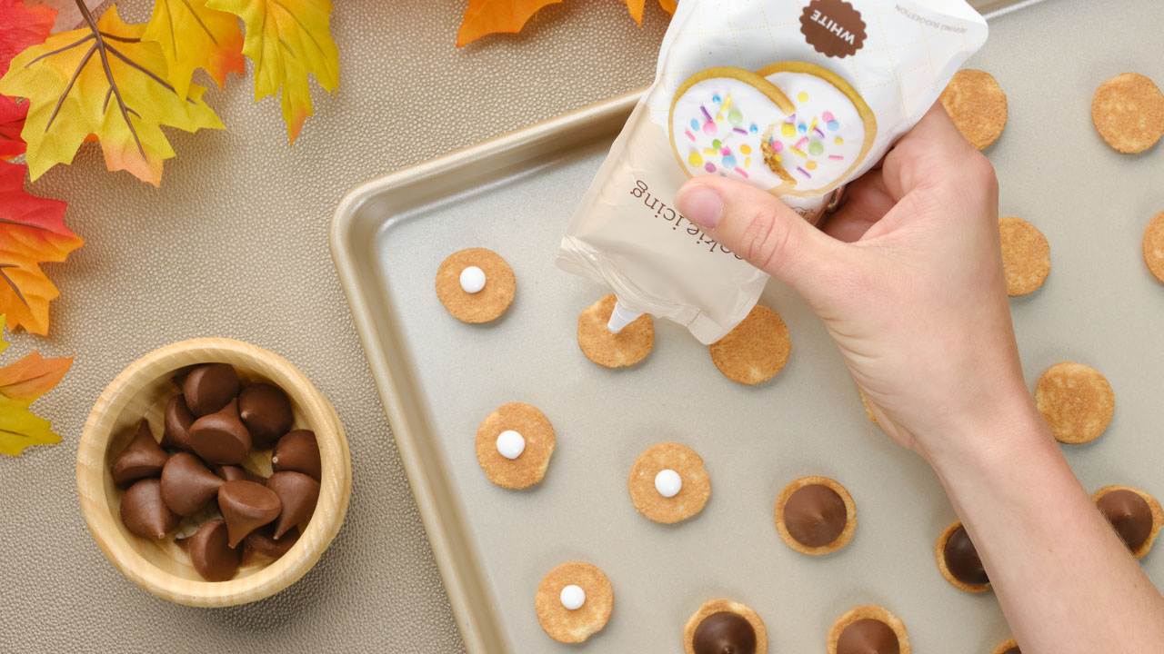 adding icing to each vanilla wafer cookie and topping with hersheys kisses milk chocolates