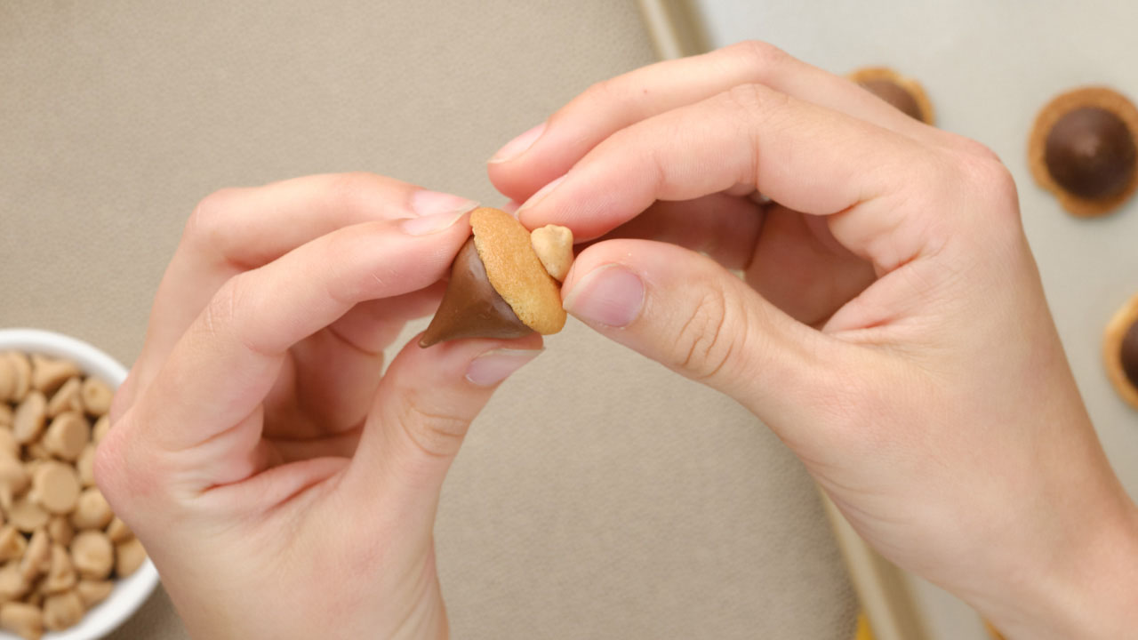 adding peanut butter baking chips to the tip of the acorn kisses treats