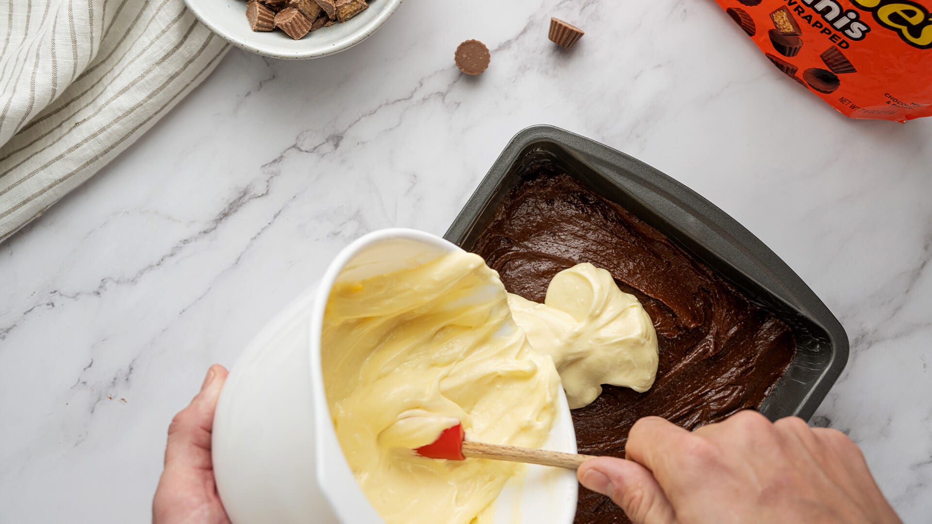 pouring cheescake batter over brownie batter 