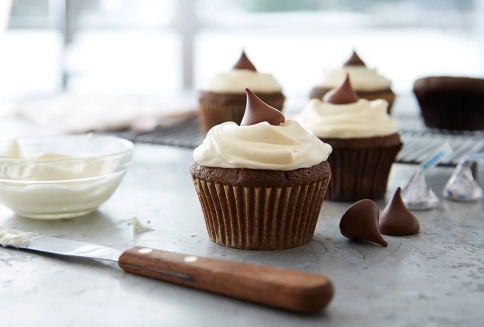 freshly baked chocolate cupcakes topped with icing and hersheys kisses