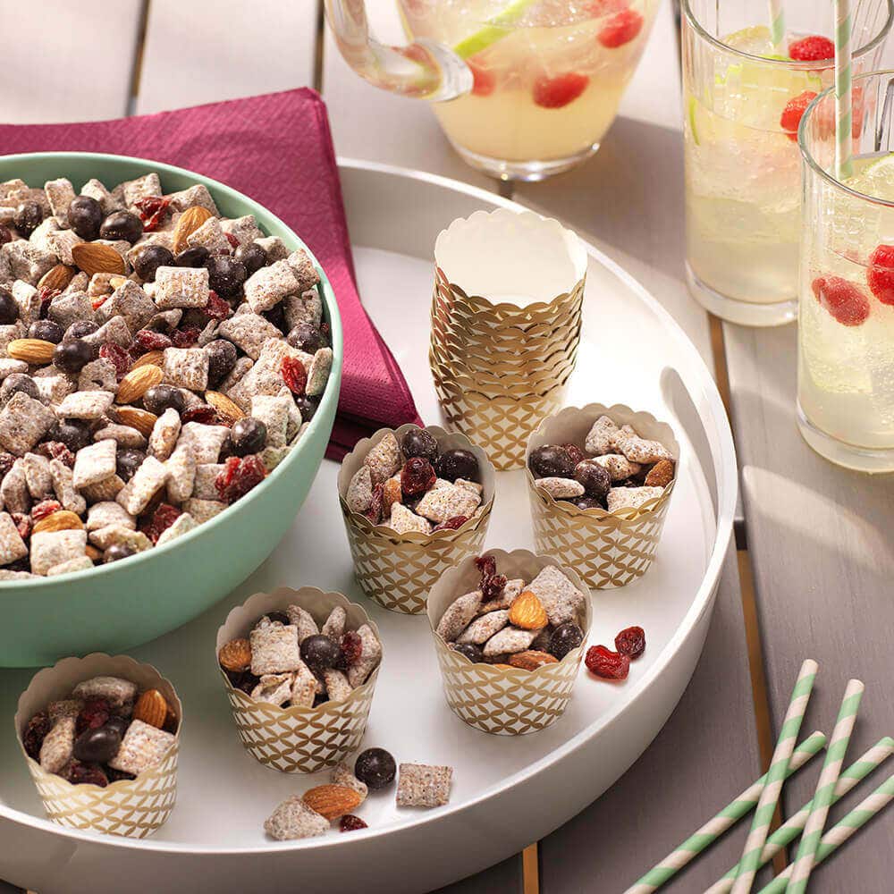 Sweet and salty party mix with chocolate, rice cereal, nuts and dried fruit, in a large bowl and divided into cups.